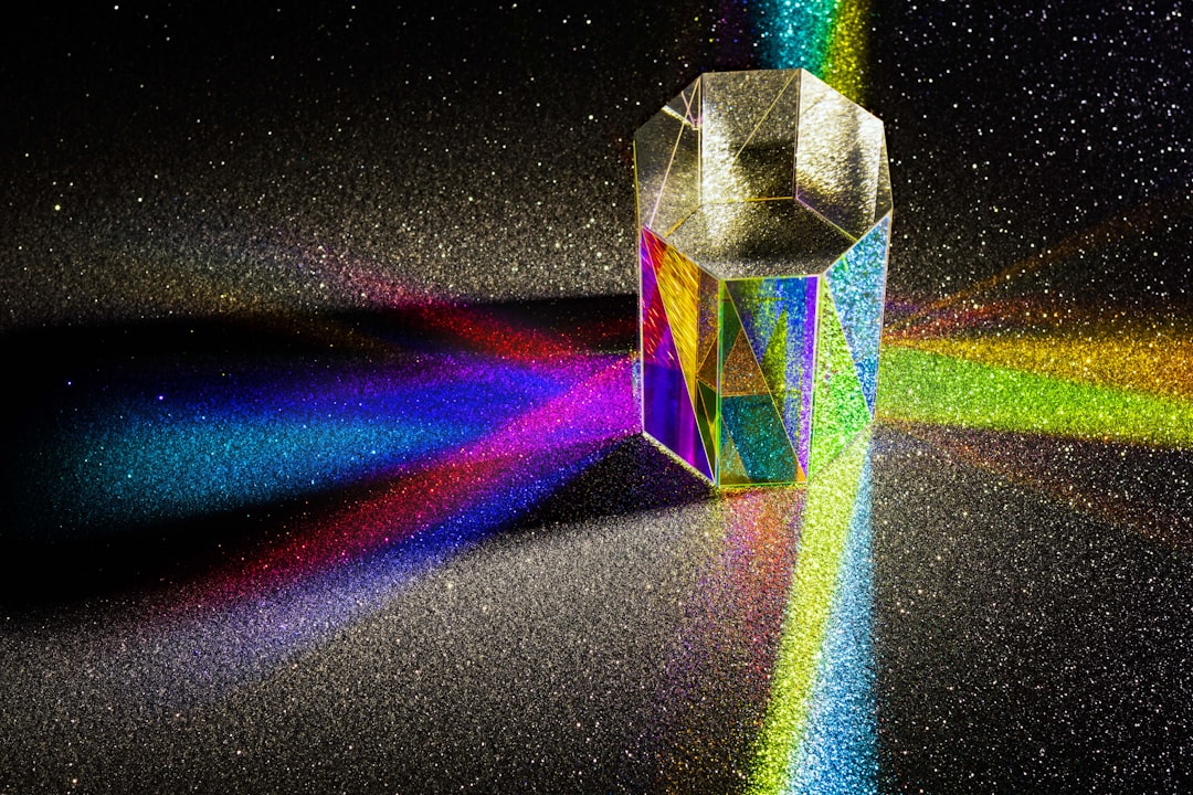 Light dispersed into rainbow colours, from an octagonal prism. The prism is placed on a black glitter background.