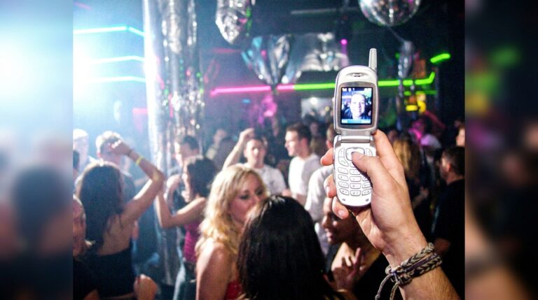 A persons hand holds up an early 2000s flip phone, y2k prompts